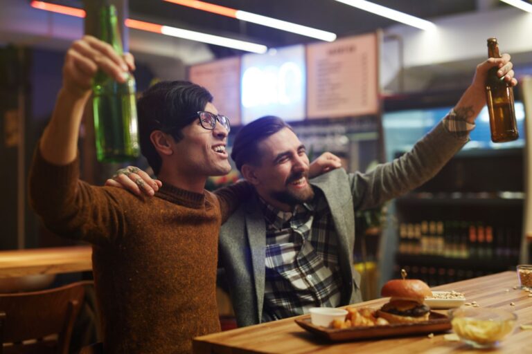 Two men enjoying drinks and food in a lively bar setting.