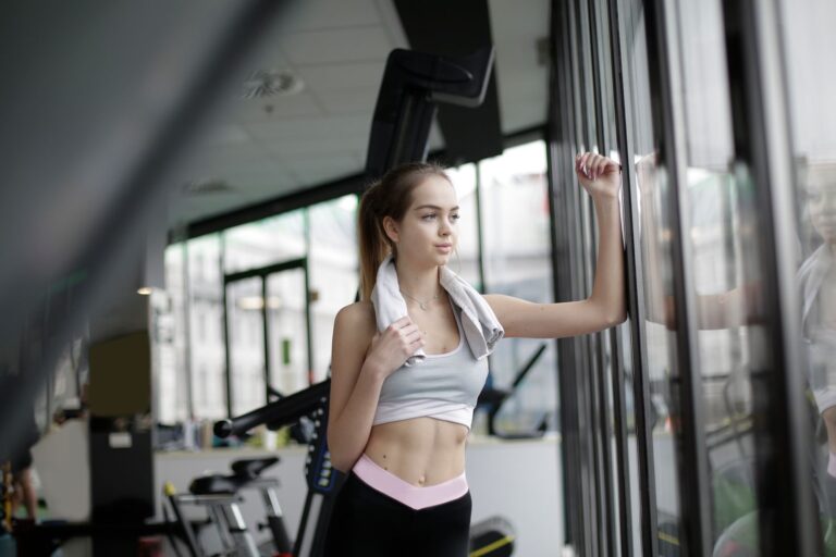 A fit woman stands by a gym window, reflecting after a workout session indoors.