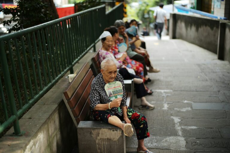 Elderly people sitting on a bench fanning themselves