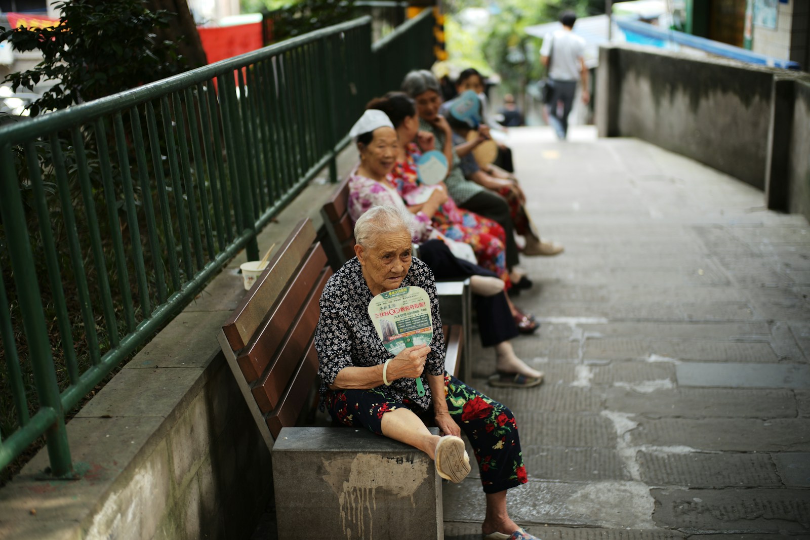 Elderly people sitting on a bench fanning themselves