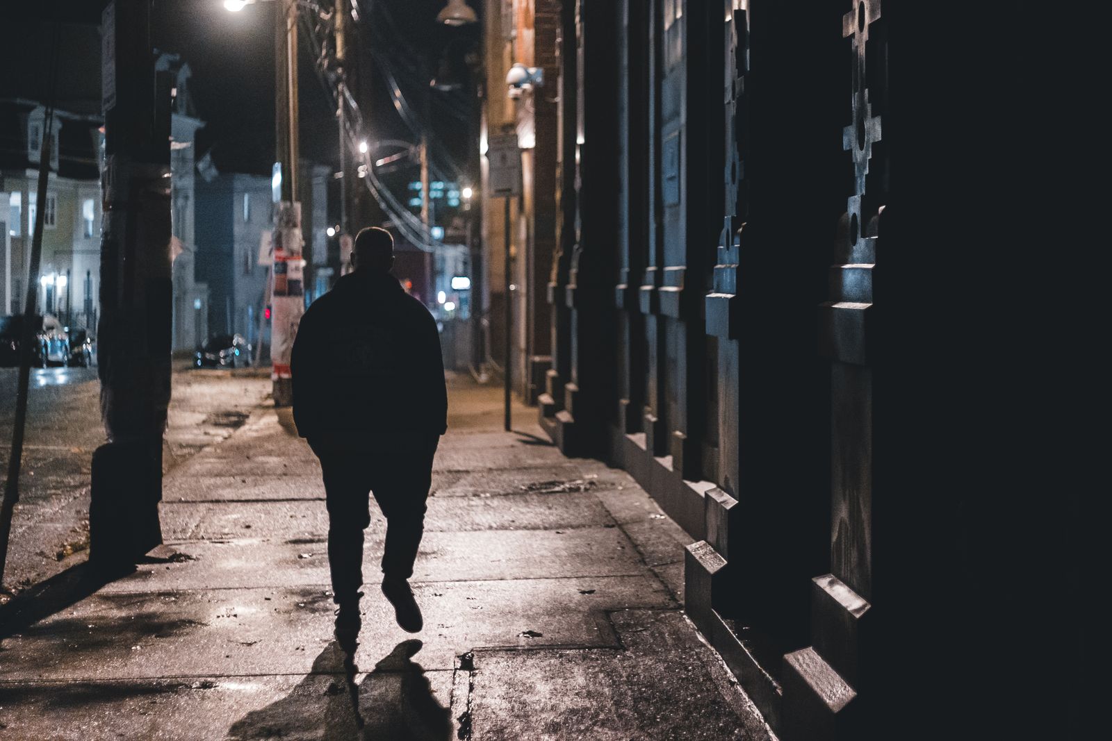 Anonymous silhouette male walking on wet sidewalk on old city street in dark night