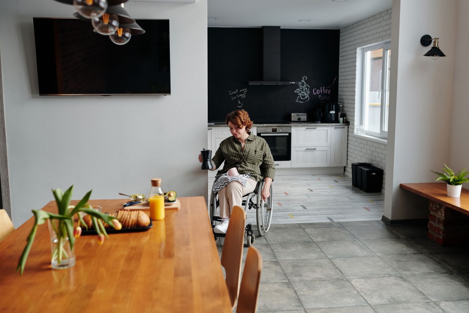 A woman in a wheelchair holding coffee in a modern kitchen setting.