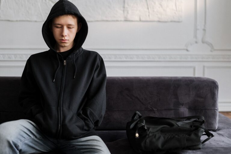 Young teen wearing hoodie sitting pensively on couch indoors.