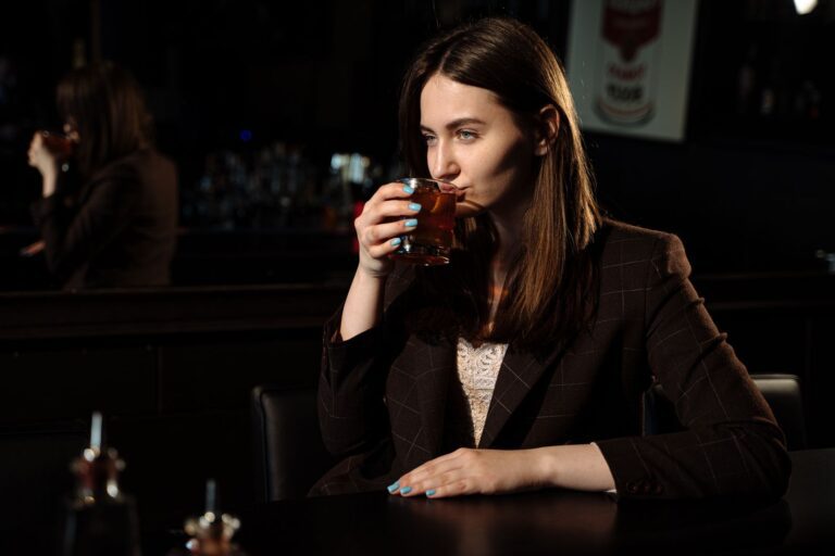Stylish woman in a dark blazer savoring a cocktail at an intimate bar setting.