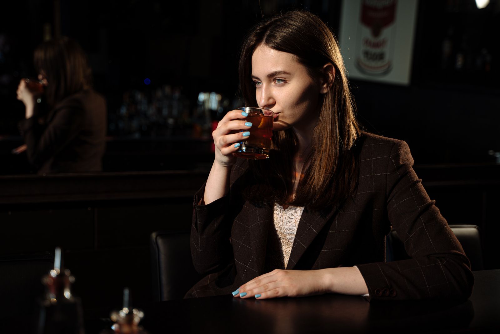 Stylish woman in a dark blazer savoring a cocktail at an intimate bar setting.