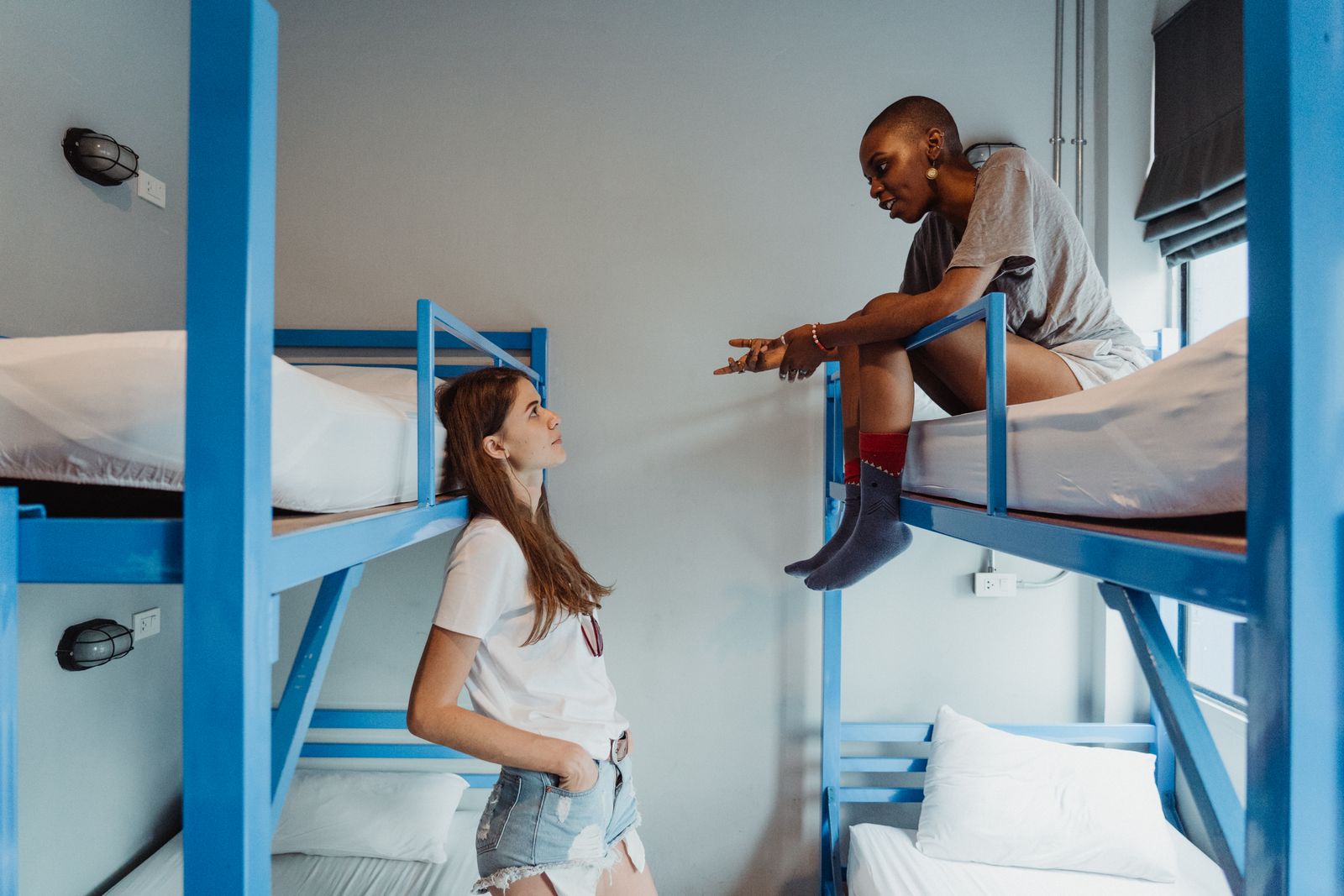 Two women engaging in conversation on bunk beds in a modern dormitory room.