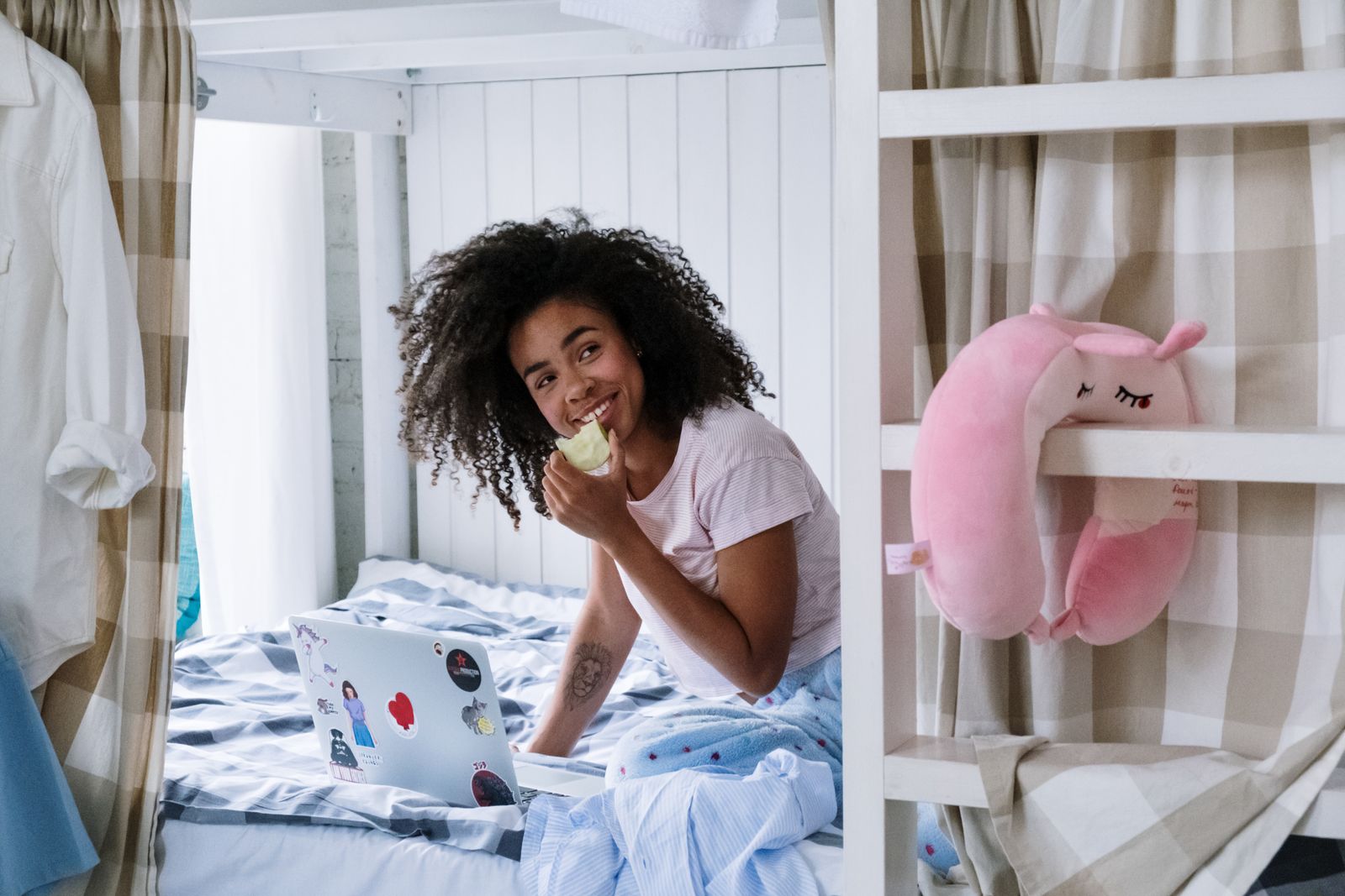 Smiling woman enjoys a cozy morning with her laptop and apple on a bed.