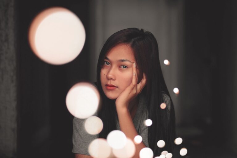 Pensive Asian female with long hair decorated with glowing lights of garland looking at camera