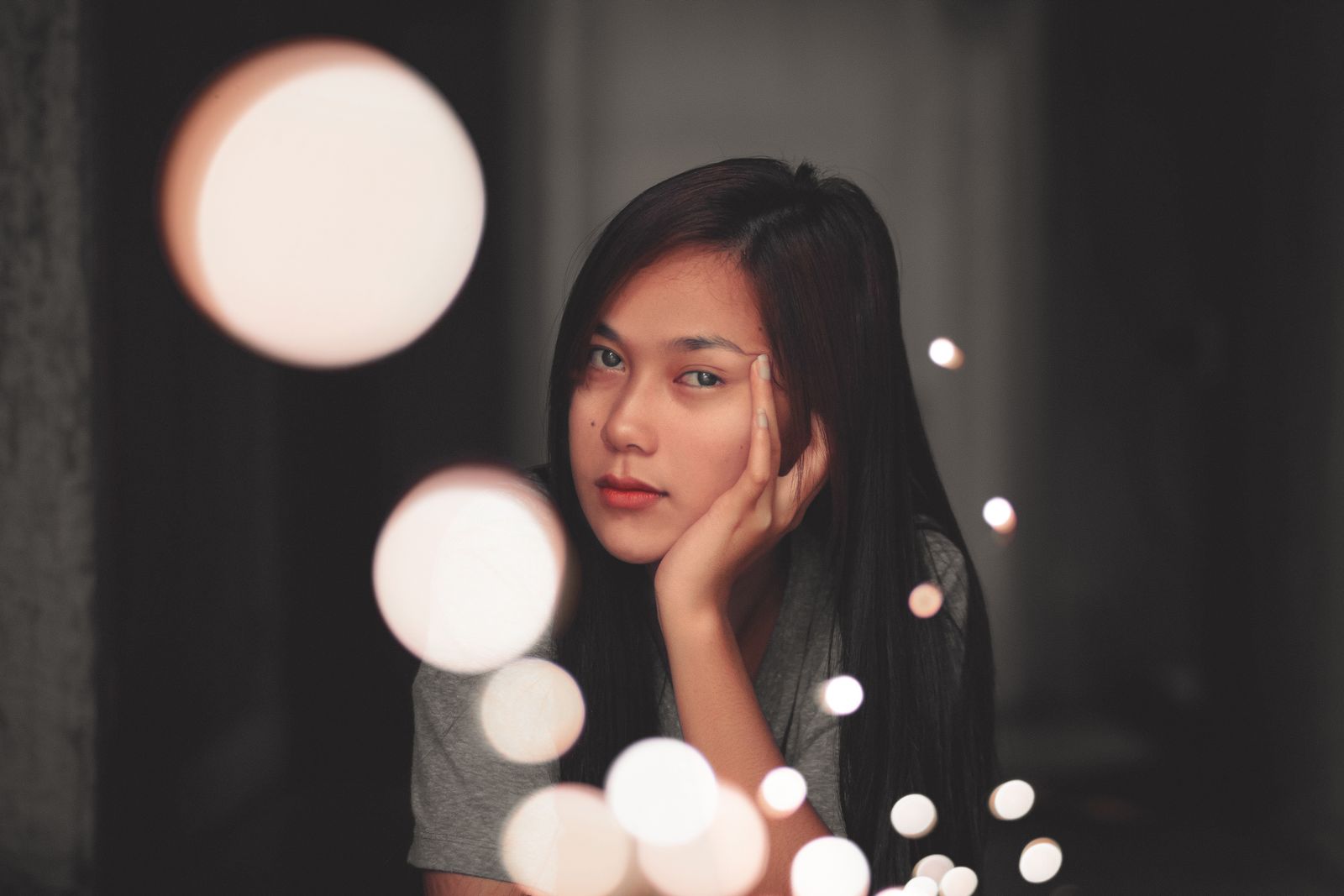 Pensive Asian female with long hair decorated with glowing lights of garland looking at camera