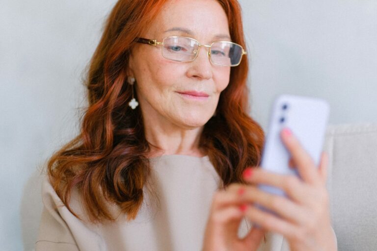 Elegant middle-aged woman with glasses using a smartphone indoors.