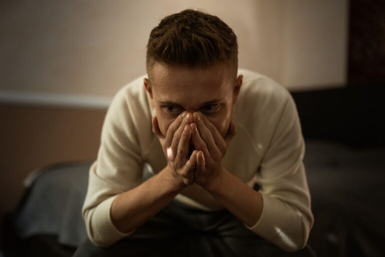 A worried man indoors covering his face with hands, depicting stress or contemplation.