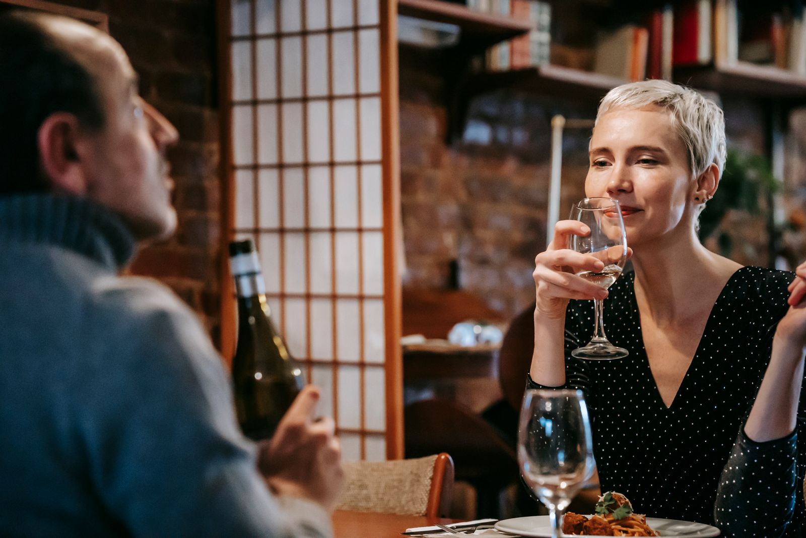 Adult couple having date in light room at table with wine in glasses and plates with pasta with meatballs near cutlery and bottle