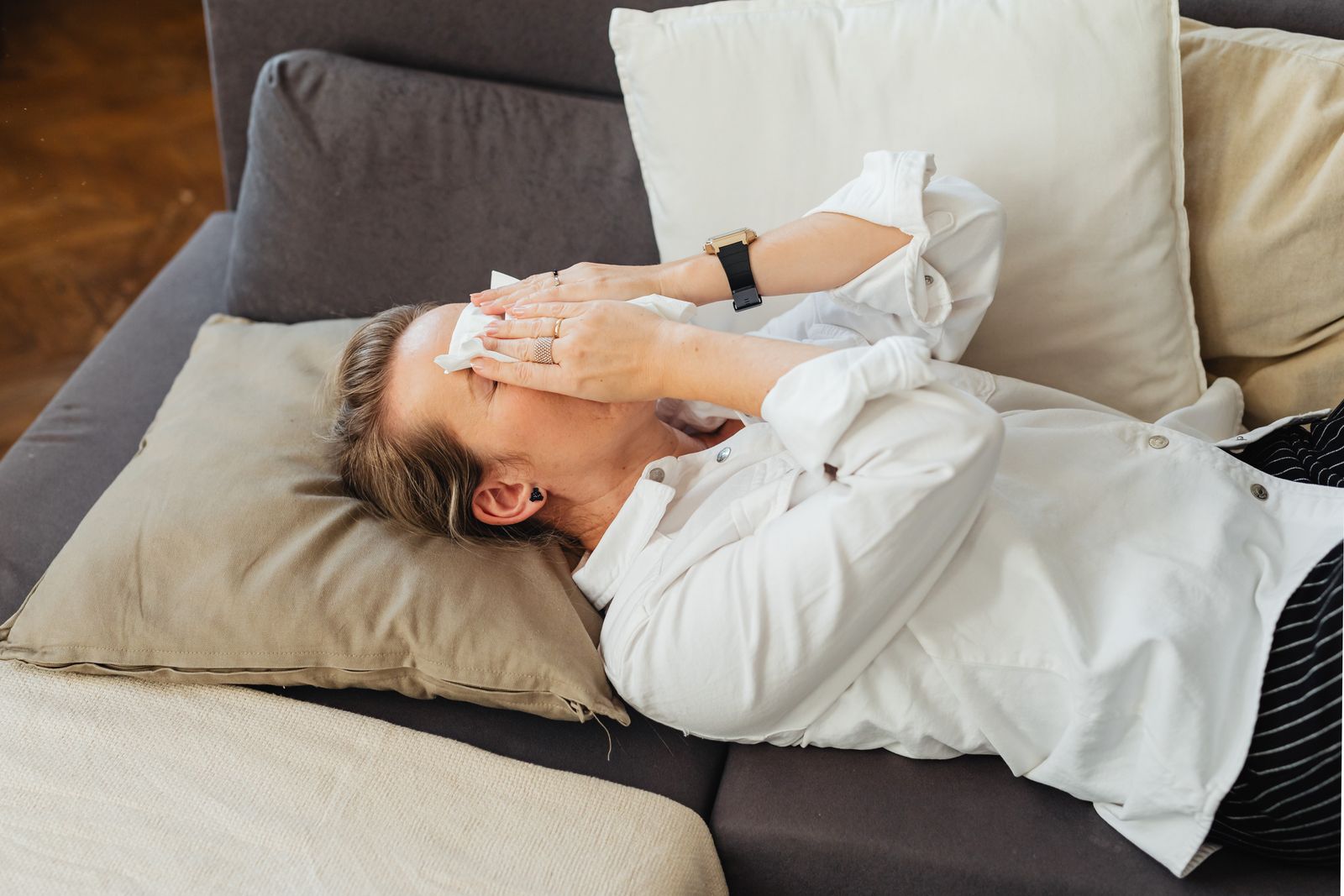 A woman lying on a couch, covering her face with a tissue, expressing sadness.