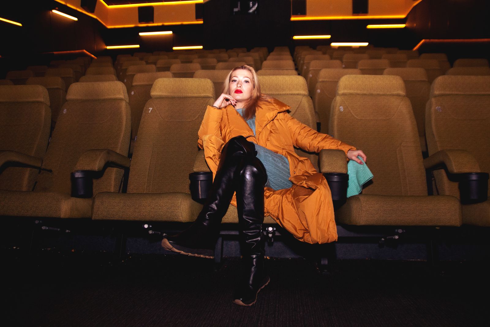 Elegant woman in a cozy theater setting, showcasing fashion with a confident pose.