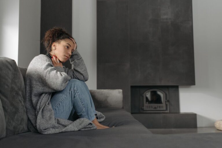 A woman in a cozy living room feeling unwell, sitting on a sofa with a thoughtful expression.
