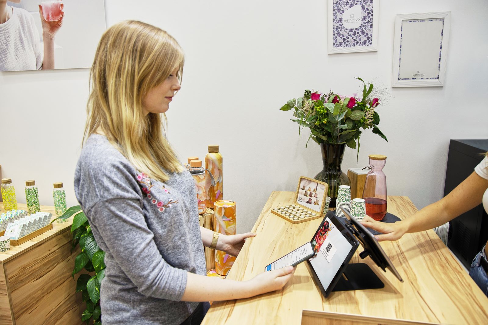 A woman uses a tablet to make a payment in a stylish Berlin store, featuring modern decor and eco-friendly products.