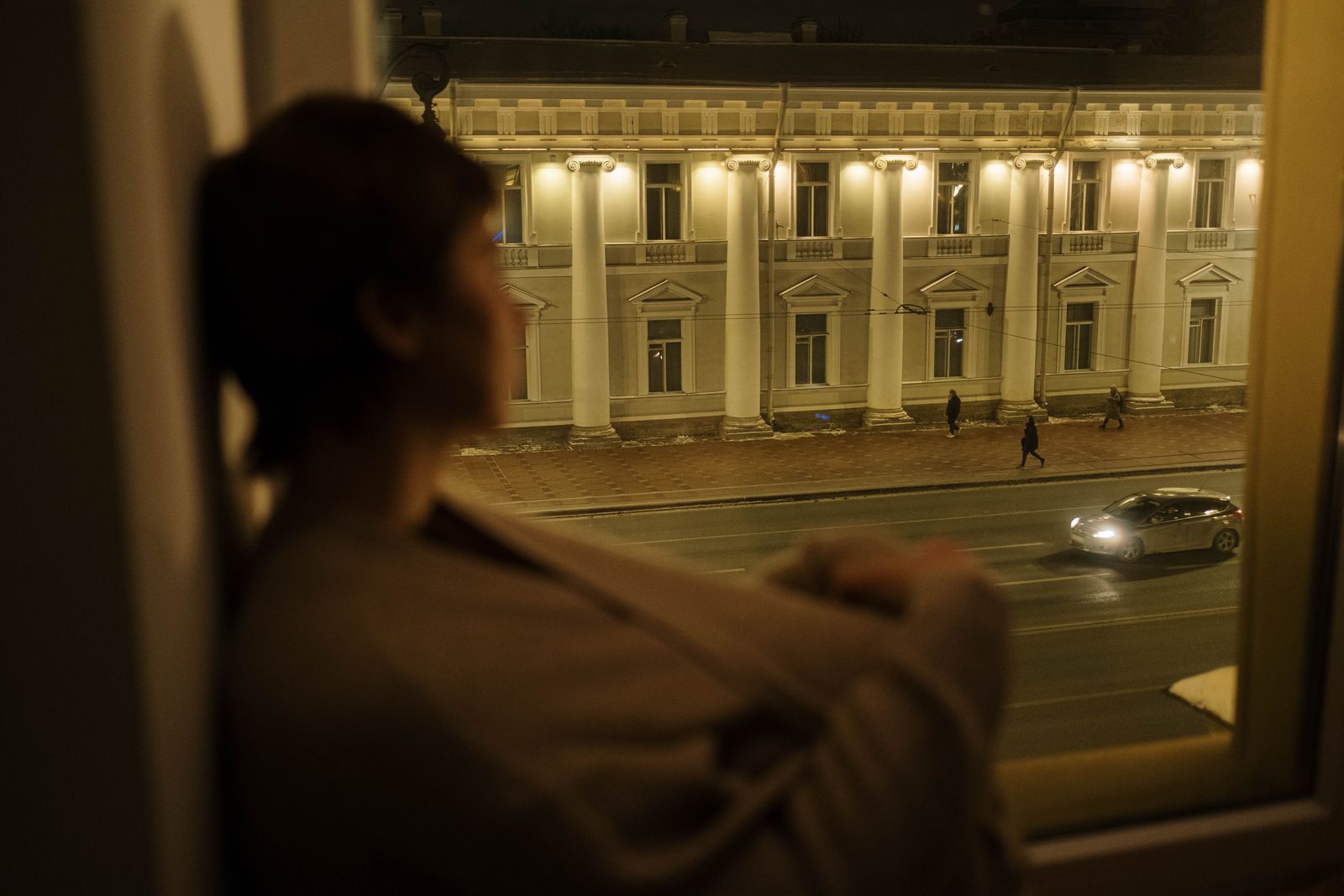 Woman gazing out a window at a city street at night, creating a serene, introspective mood.