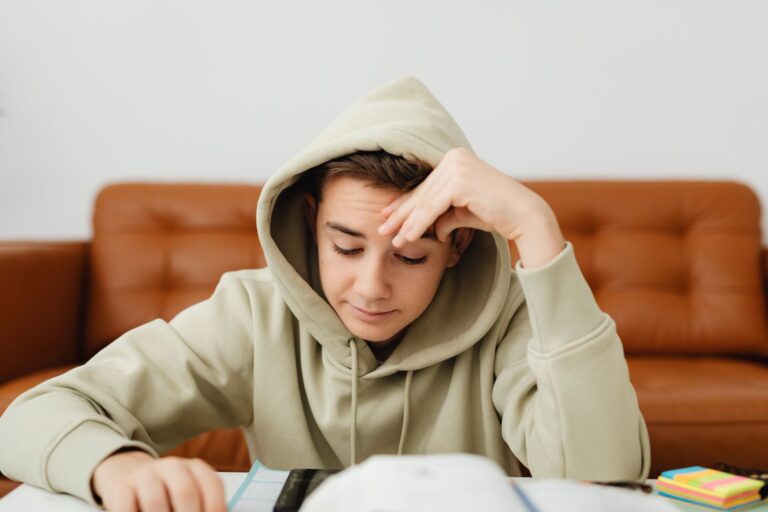 Teenage boy in a hoodie focused on studying, sitting indoors at a table.