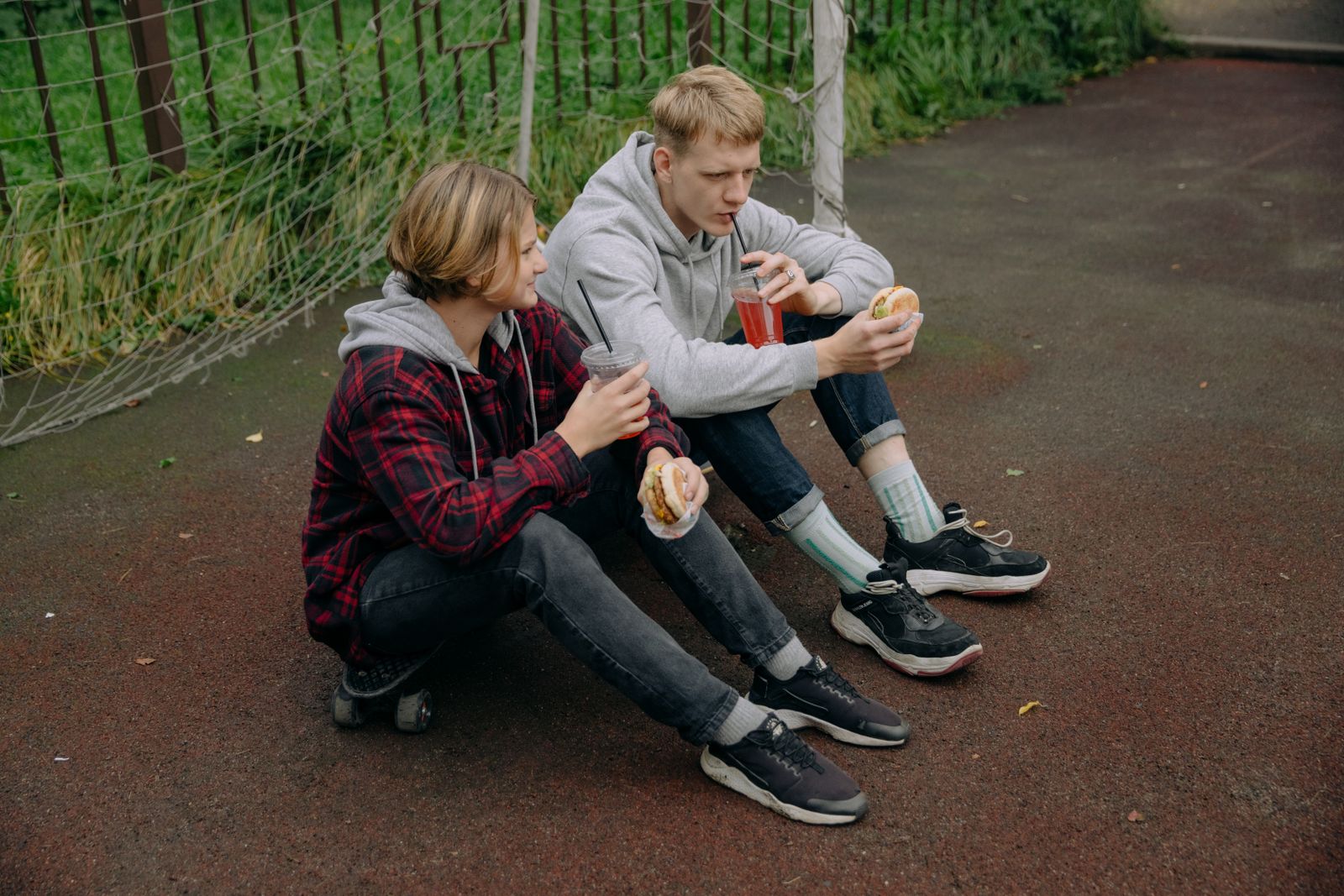 Two teenagers sitting outdoors, enjoying burgers and drinks on a casual day.