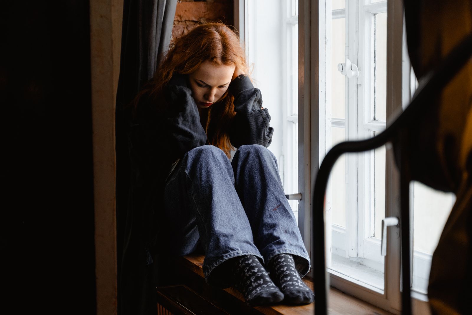 A woman sits pensively by a window, expressing feelings of solitude and contemplation.
