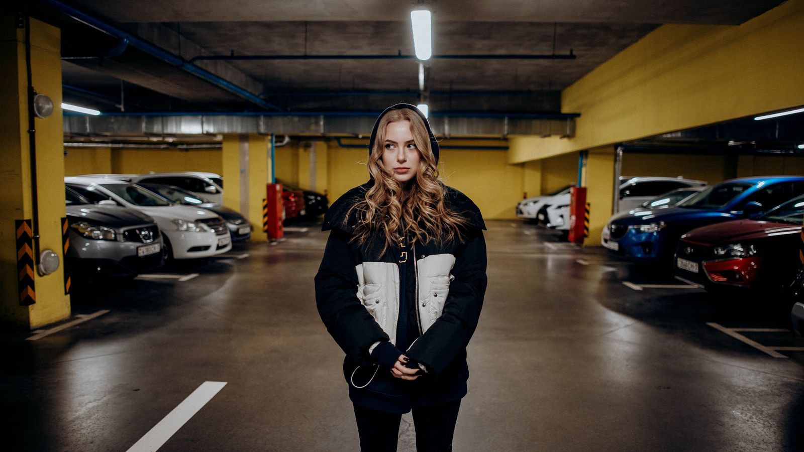 Caucasian woman standing confidently in an underground parking garage, modern casual fashion.