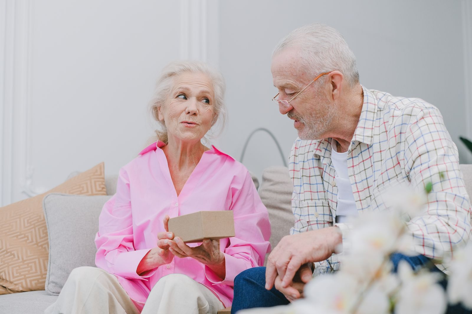 Elderly couple sitting indoors, sharing a heartfelt moment with a gift.