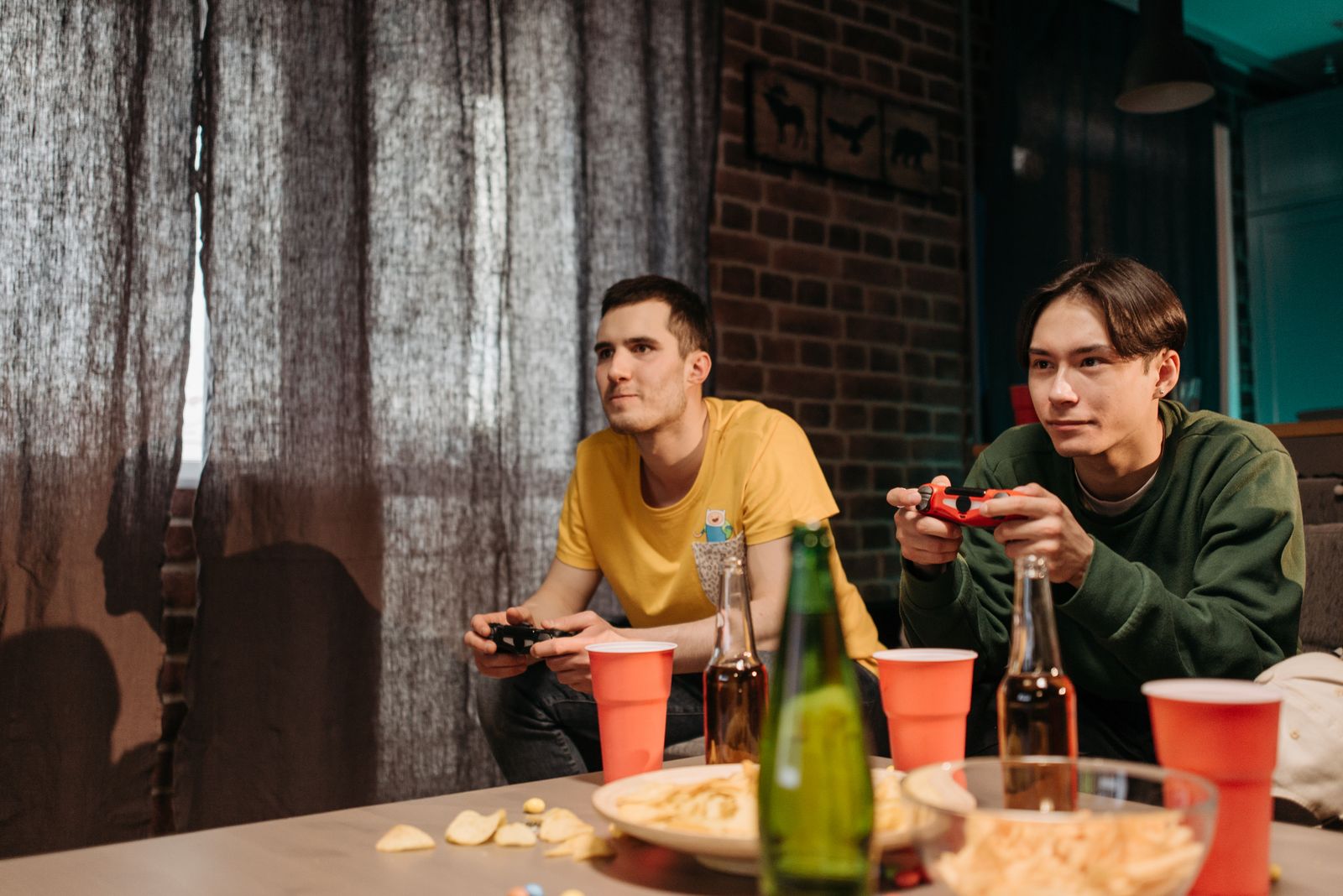 Two young men engaged in video gaming at home surrounded by snacks and drinks.