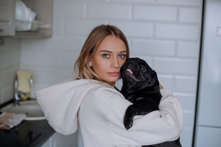 Young woman in hoodie cuddling a pug in a modern kitchen setting. Warm and cozy feeling.