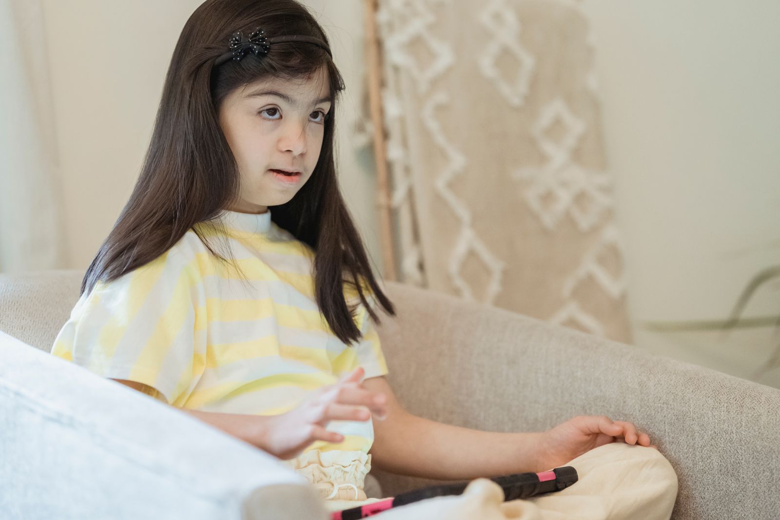A young girl with Down syndrome sits on a couch in a cozy indoor setting, radiating innocence.