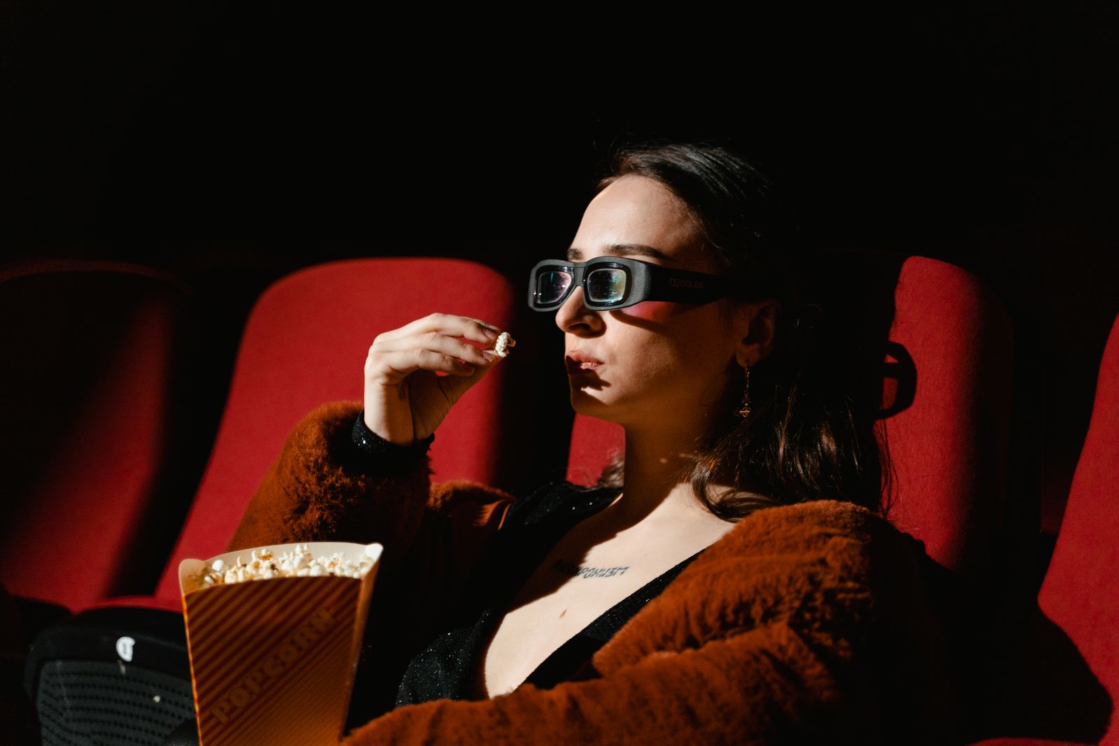 A woman enjoying a cinema experience wearing 3D glasses, holding popcorn.