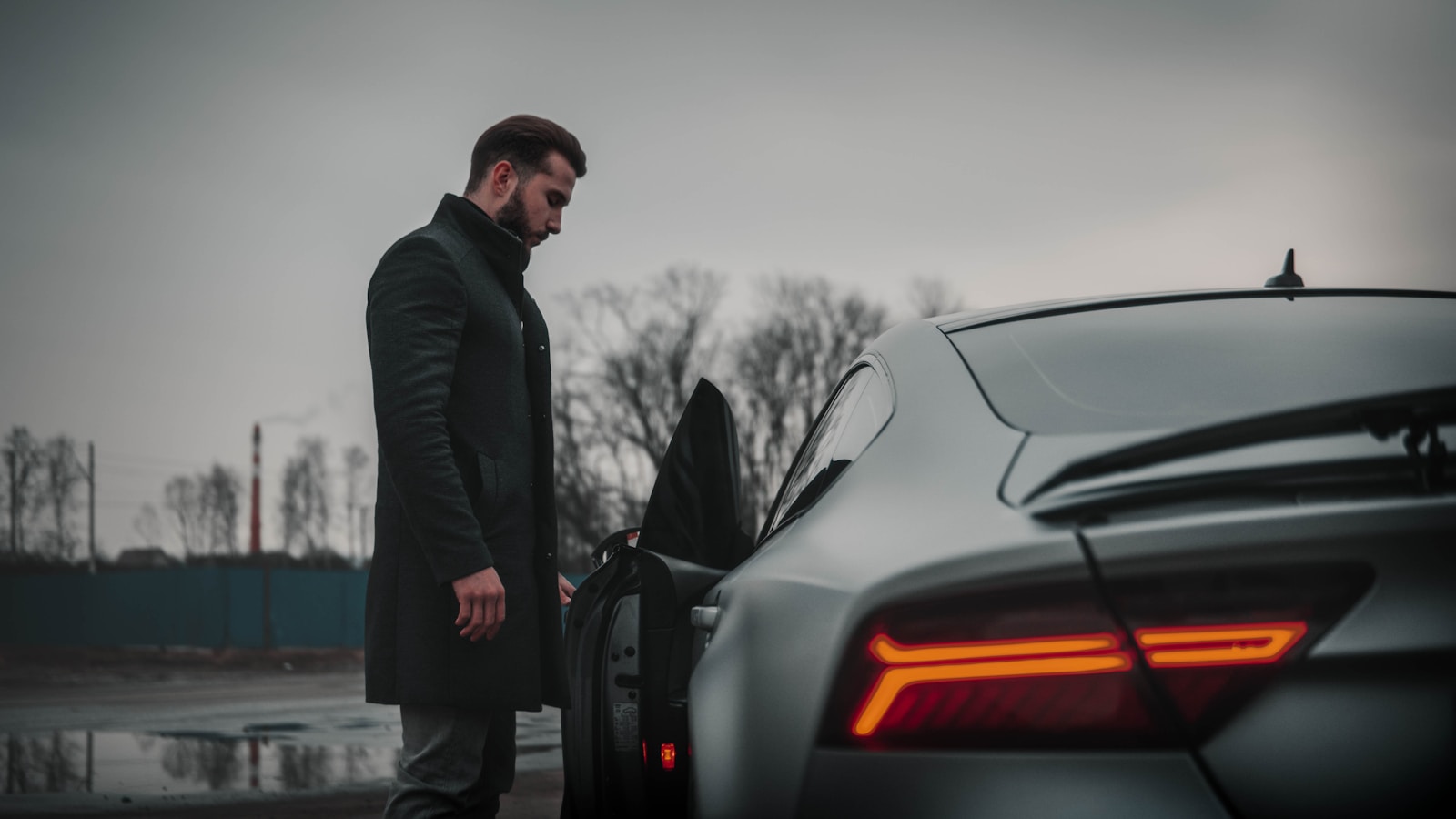 man in black jacket standing beside black car during daytime