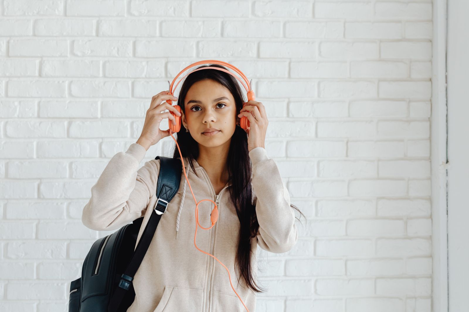 Teen girl wearing headphones and a backpack against a brick wall background.