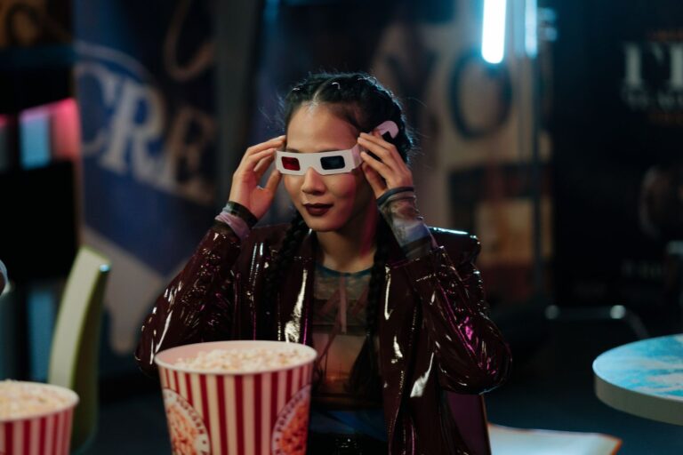 Woman in a cinema wearing 3D glasses and enjoying popcorn, movie night ambiance.
