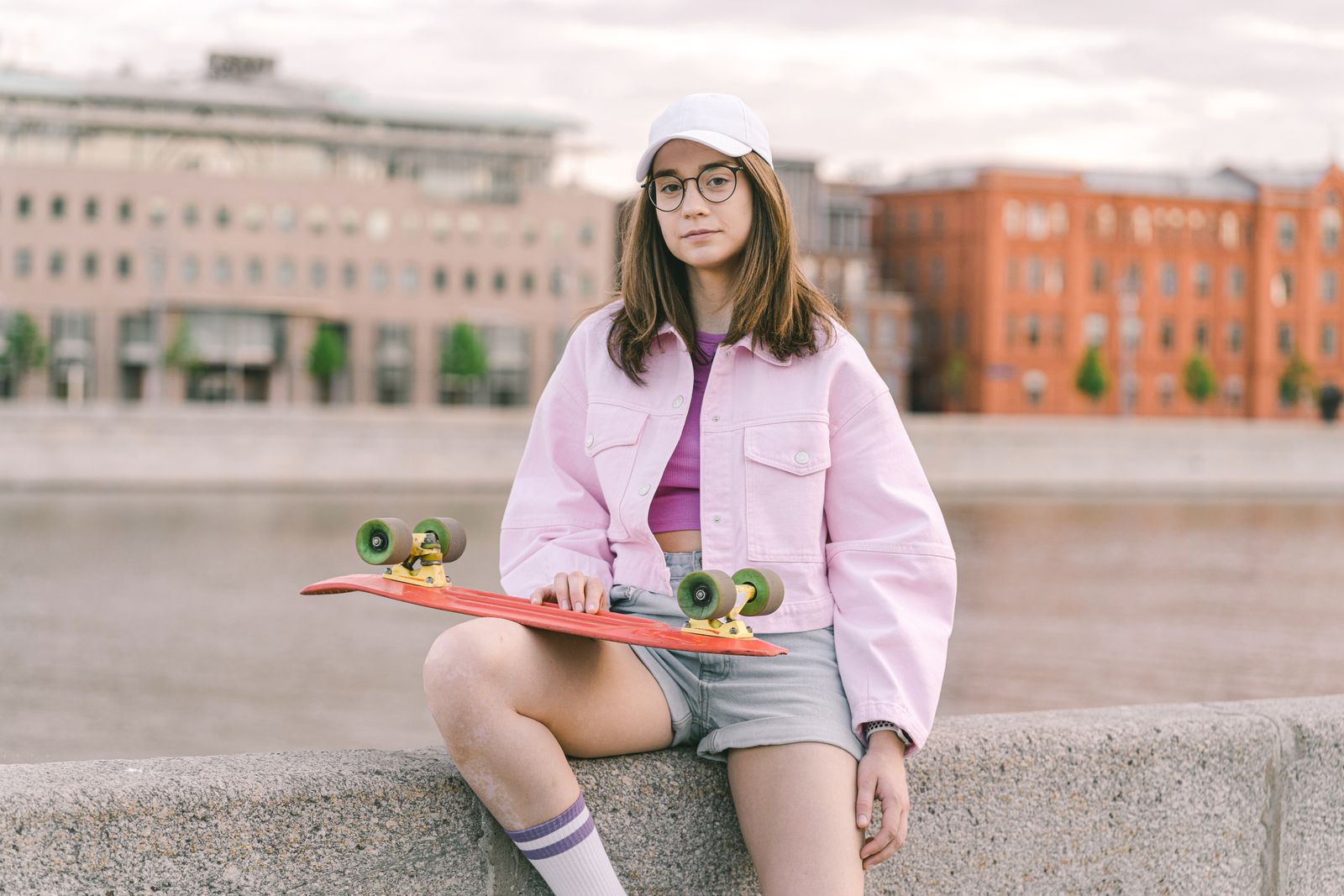 Portrait of a young woman in casual wear holding a skateboard outdoors.