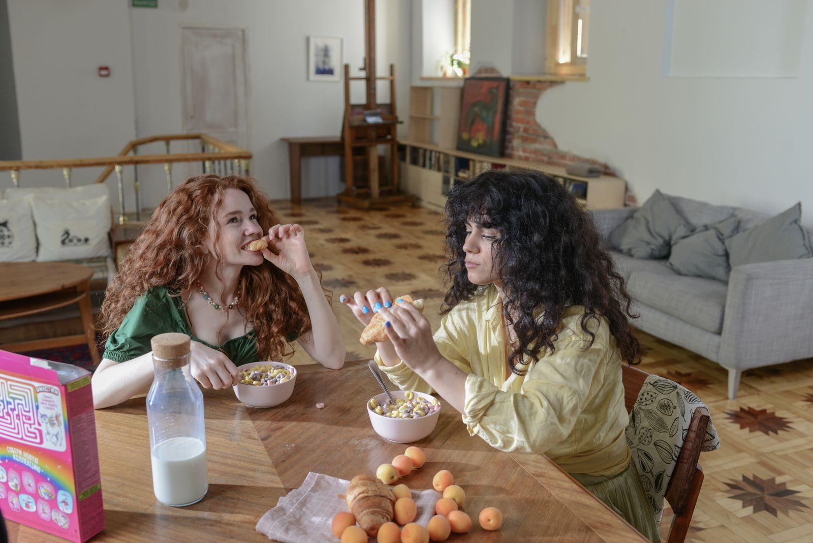 Two women enjoying a relaxed breakfast with cereal and fruit in a cozy home setting.