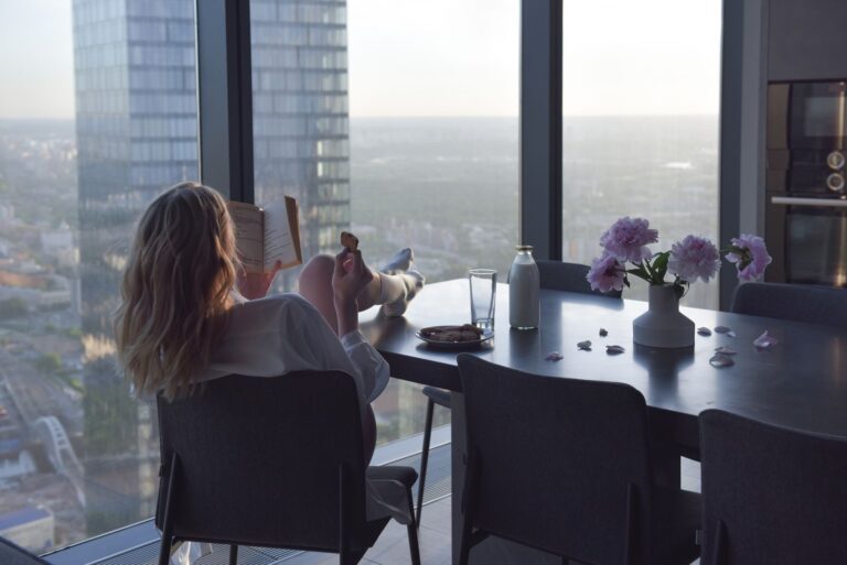 Woman enjoying a book by a window with city view, in a modern indoor setting.