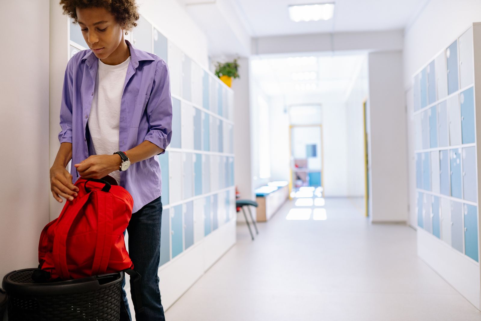A young student organizing his backpack in a bright school hallway.