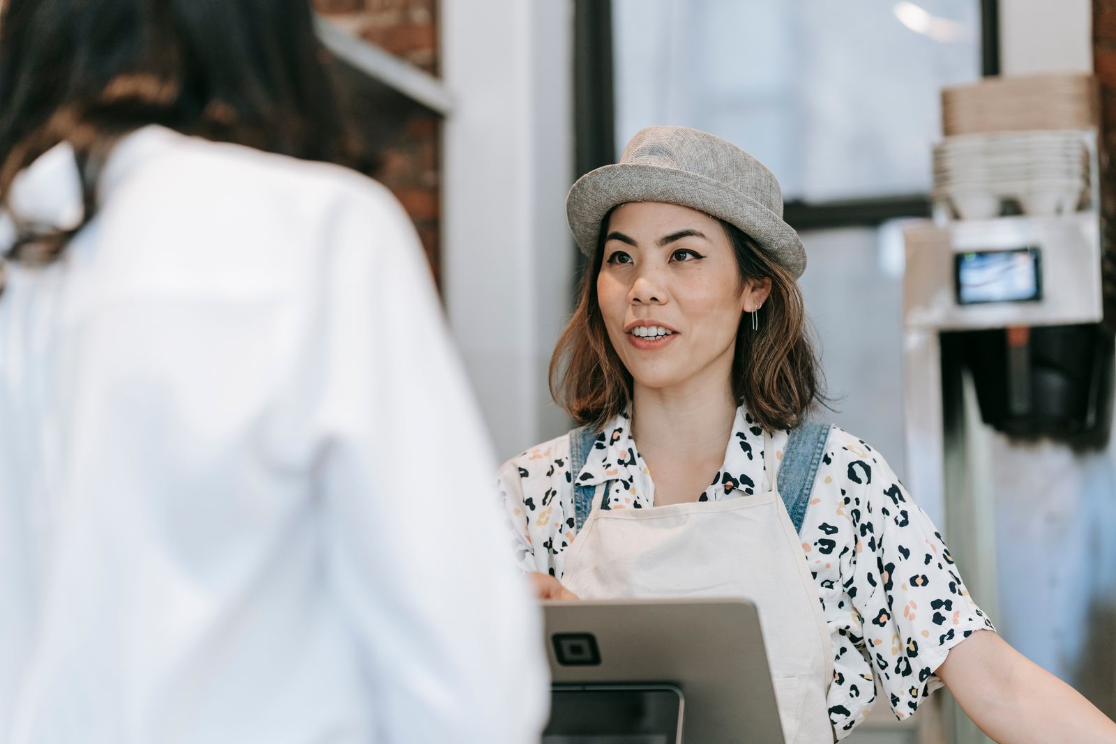 A cheerful barista in a hat takes an order from a customer at a cozy coffee shop counter.