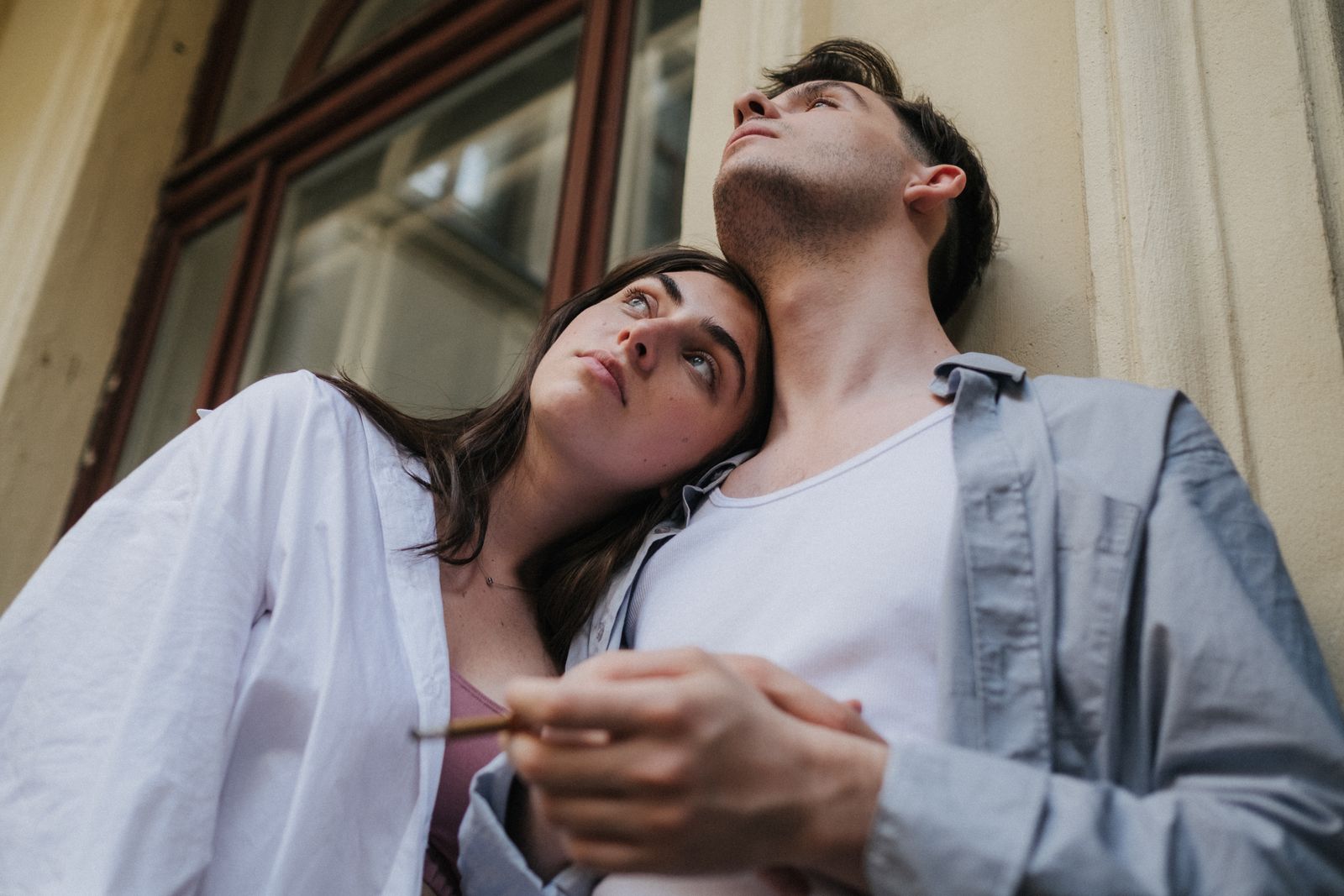 A couple leans affectionately on a balcony, gazing upwards in a relaxed outdoor setting.