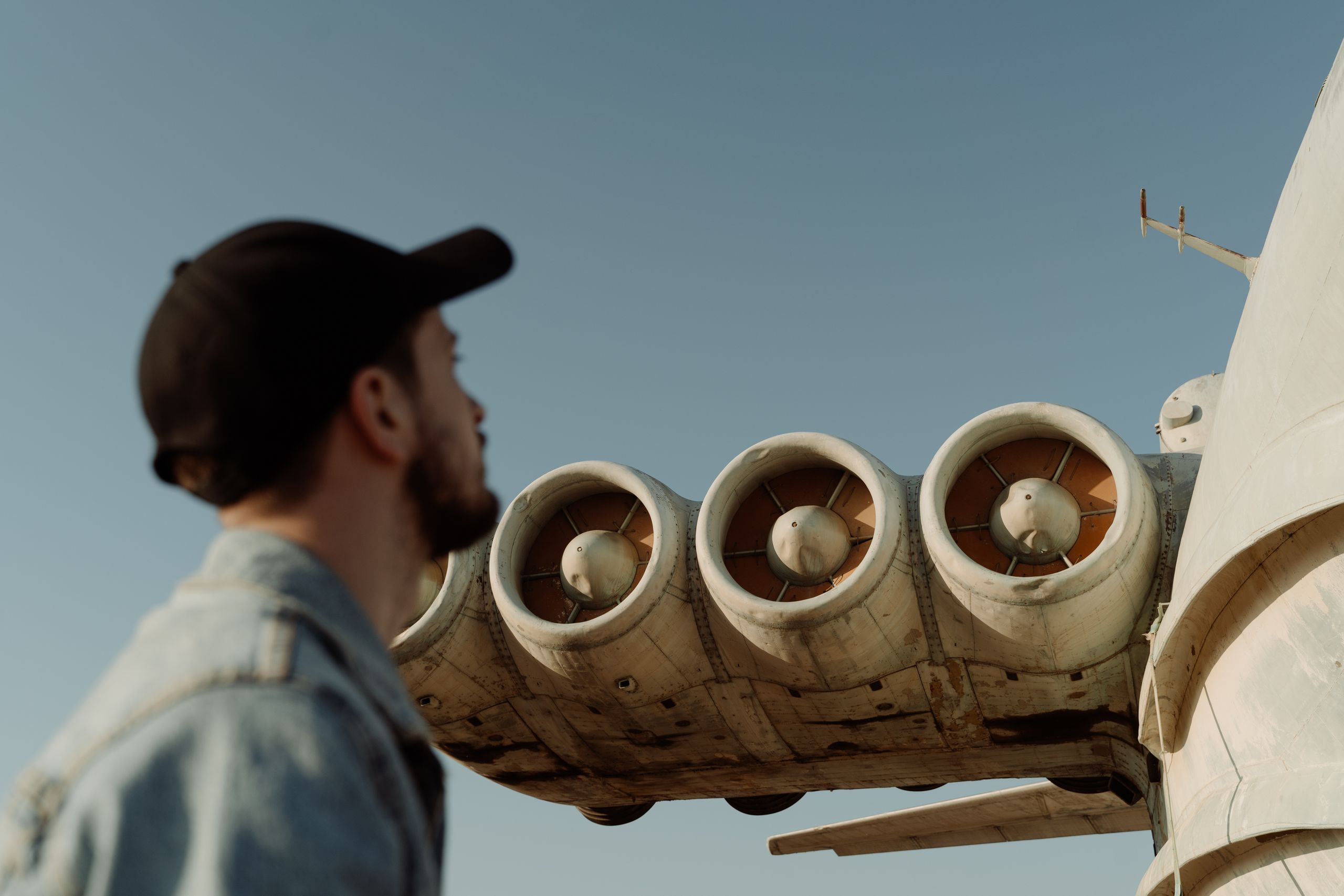 A man in a cap looks at the airplane engine against a blue sky, depicting aviation interest.