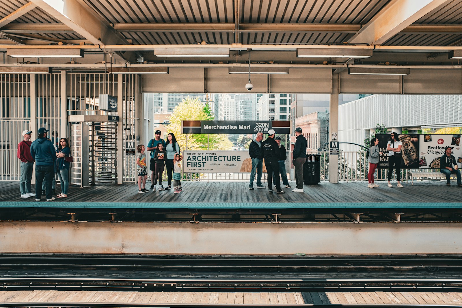 People waiting on a train platform with tracks and buildings.