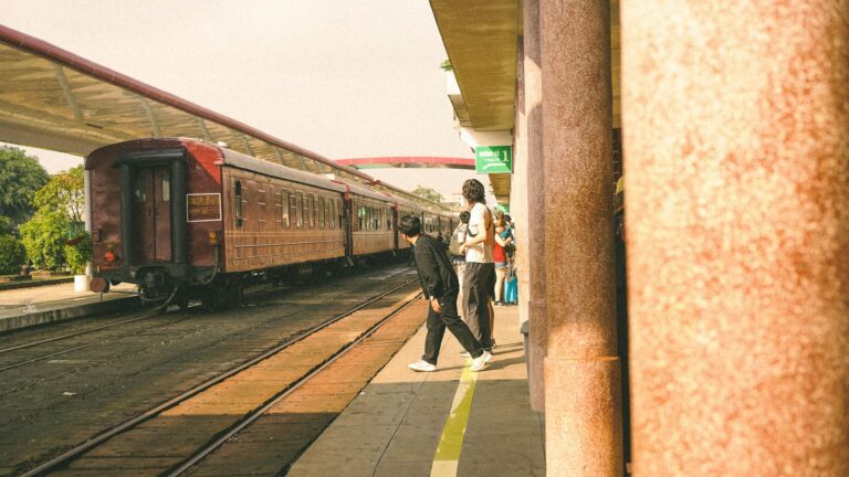 Two people crossing train tracks at a station