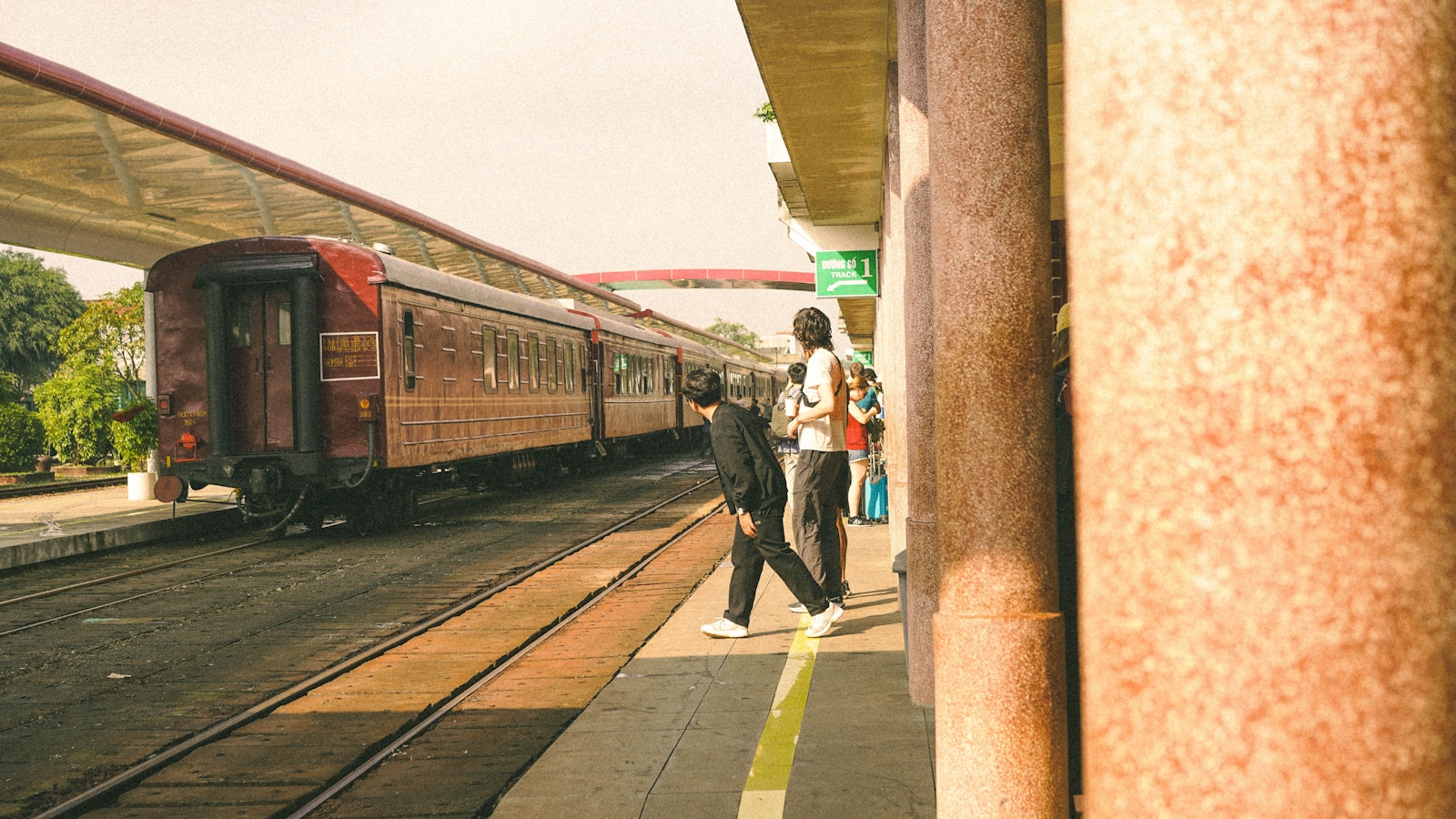 Two people crossing train tracks at a station