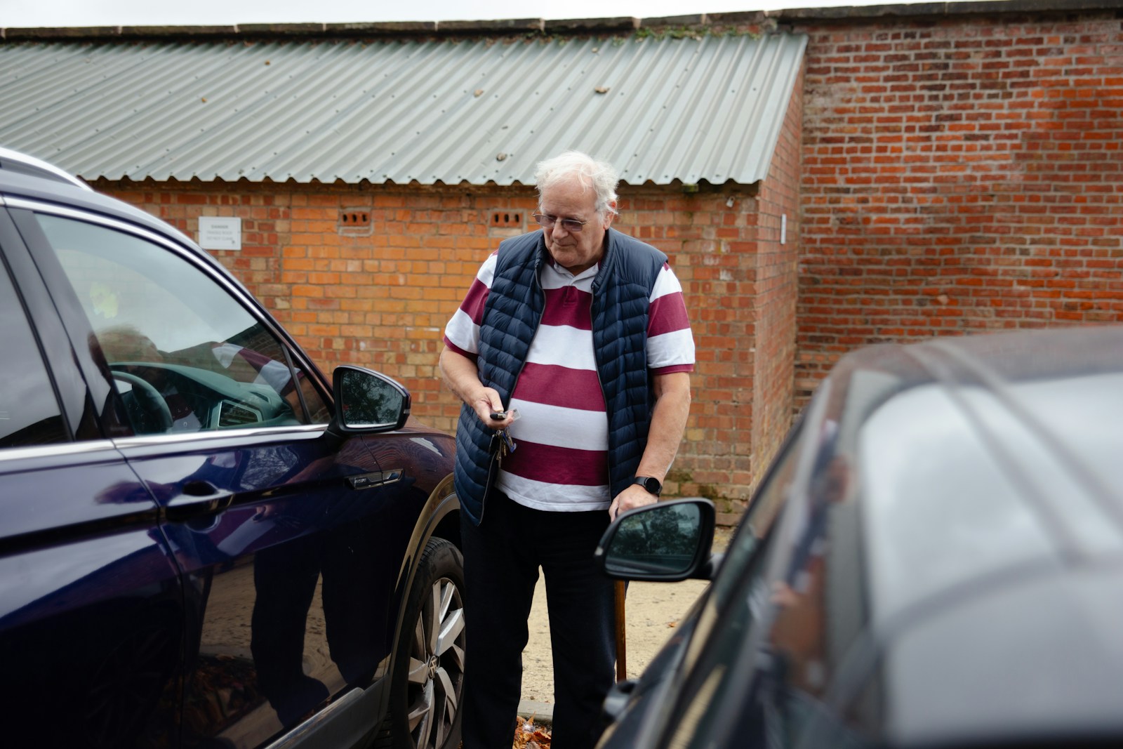 An older man stands between two cars