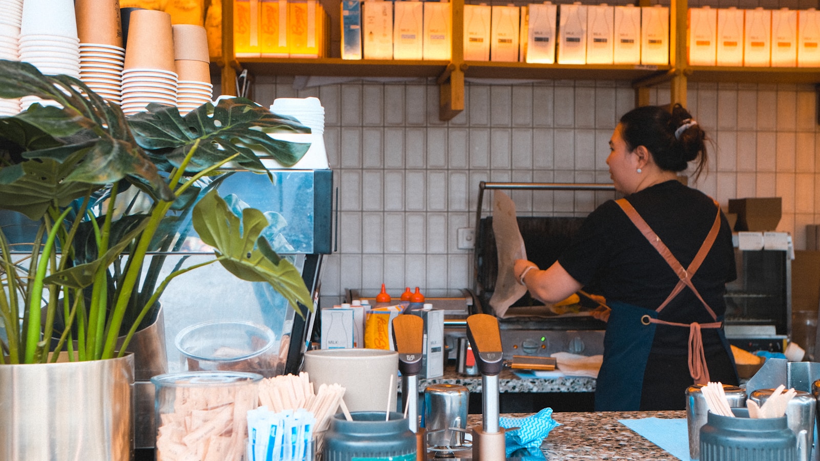 Barista preparing drinks behind a counter with plants.
