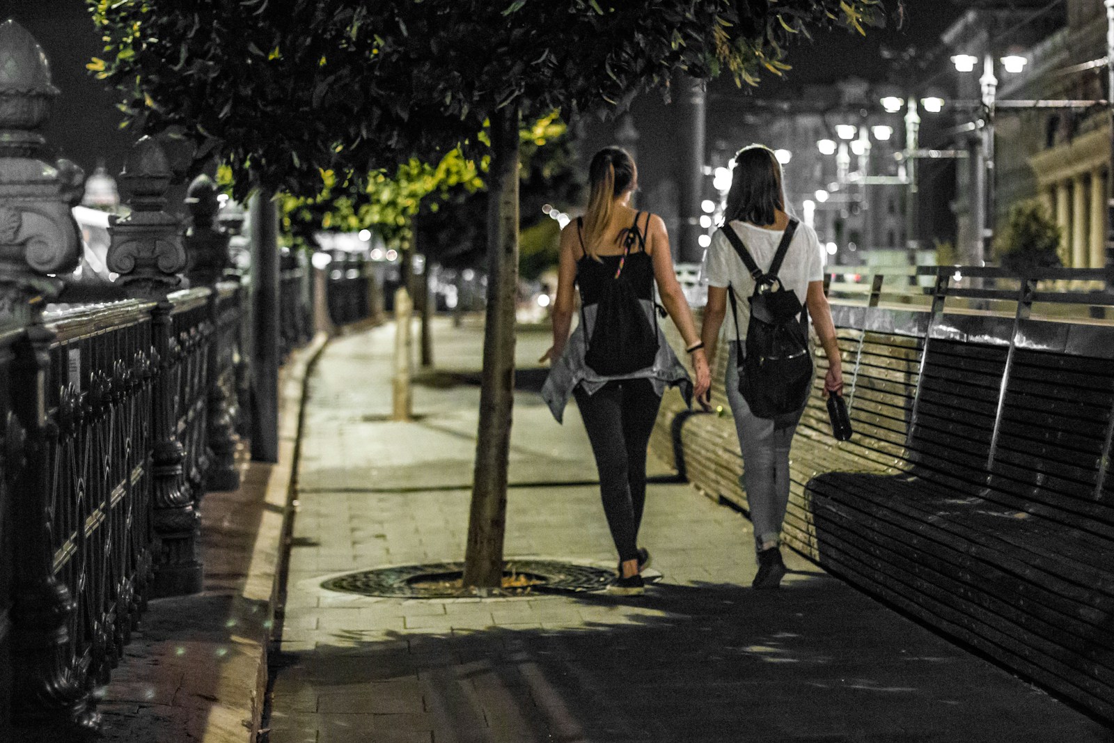 Two friends hold hands while walking at night.