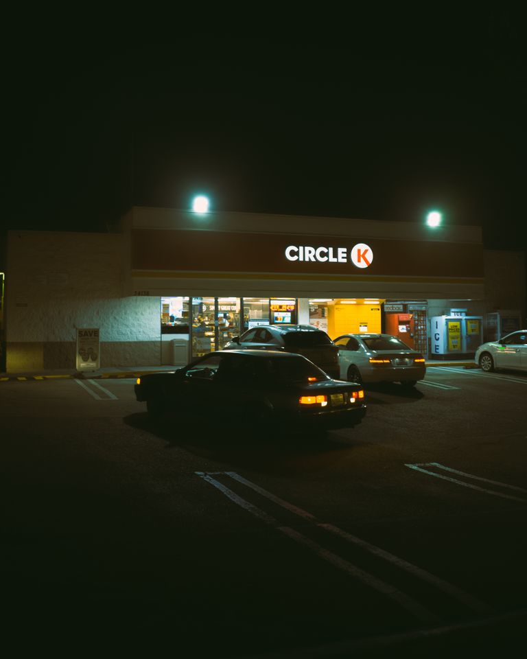Parking lot with cars near illuminated sign of store with glowing lights at night time on street in dark city