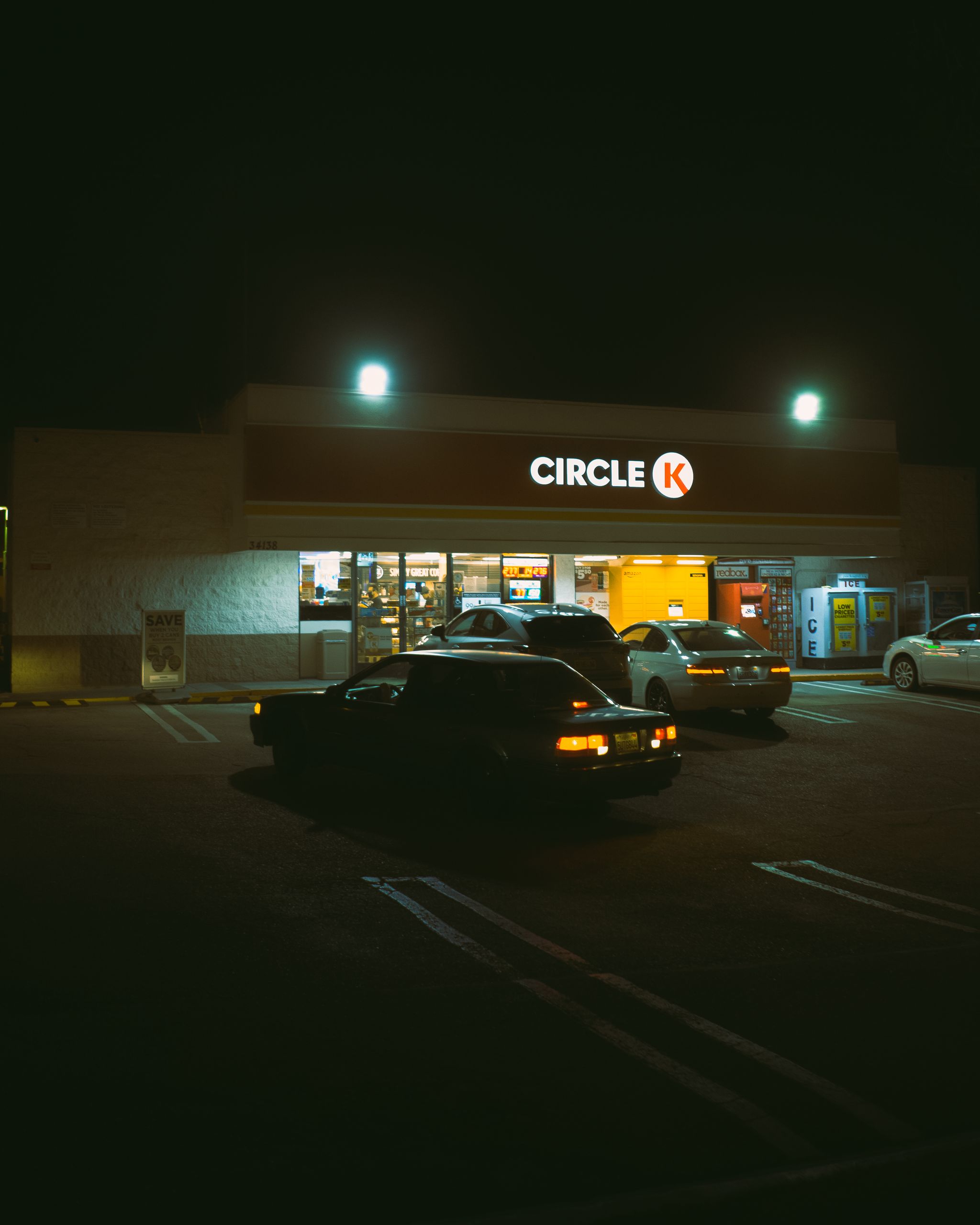 Parking lot with cars near illuminated sign of store with glowing lights at night time on street in dark city