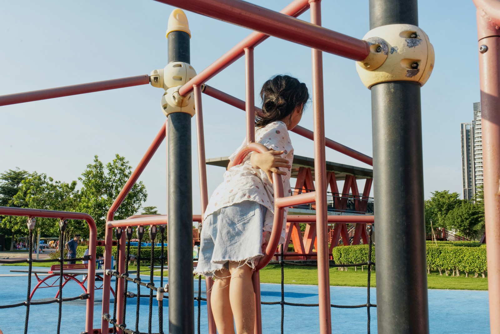 girl in white dress standing on red metal bar during daytime