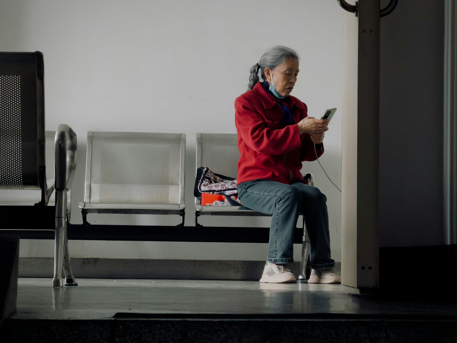 Elderly woman in red jacket uses smartphone while sitting.